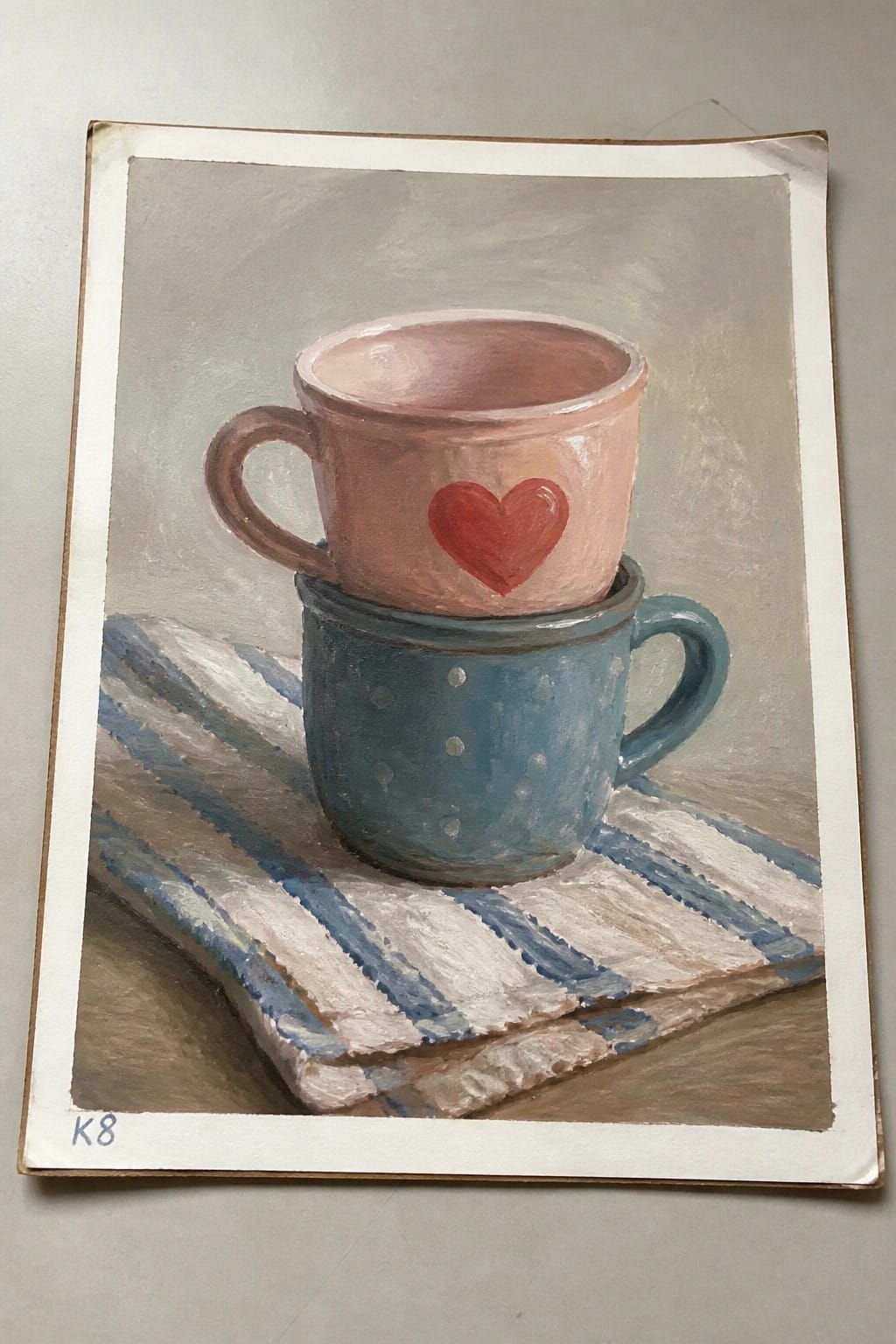 Stacked pink heart mug atop blue dotted mug on striped cloth painting