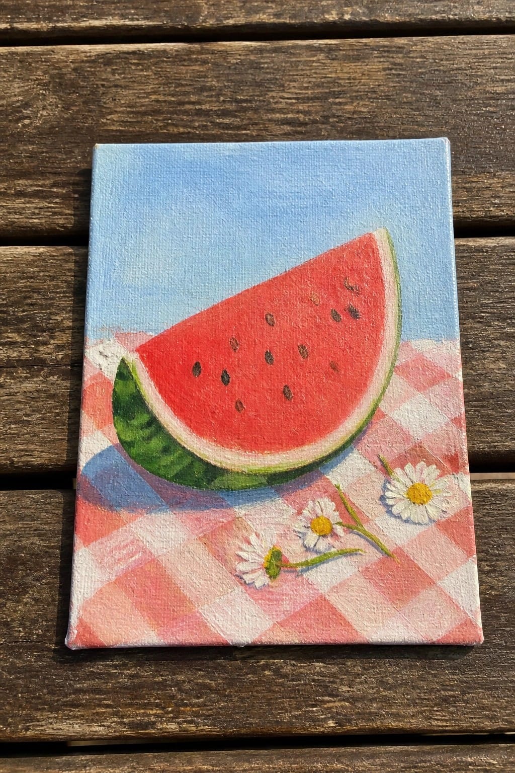 Watermelon slice on red checkered cloth with daisies against blue sky