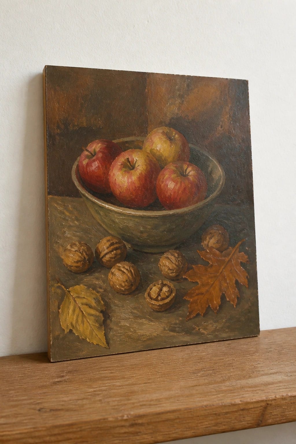 Still life painting of apples in bowl with walnuts and autumn leaves on wood.