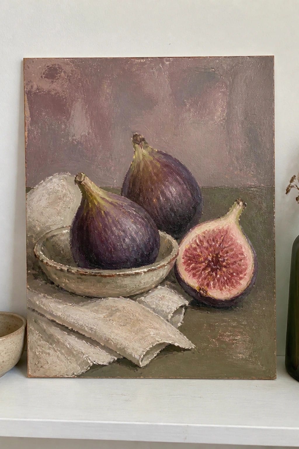 Still life painting of three purple figs, one halved, in a bowl with cloth.