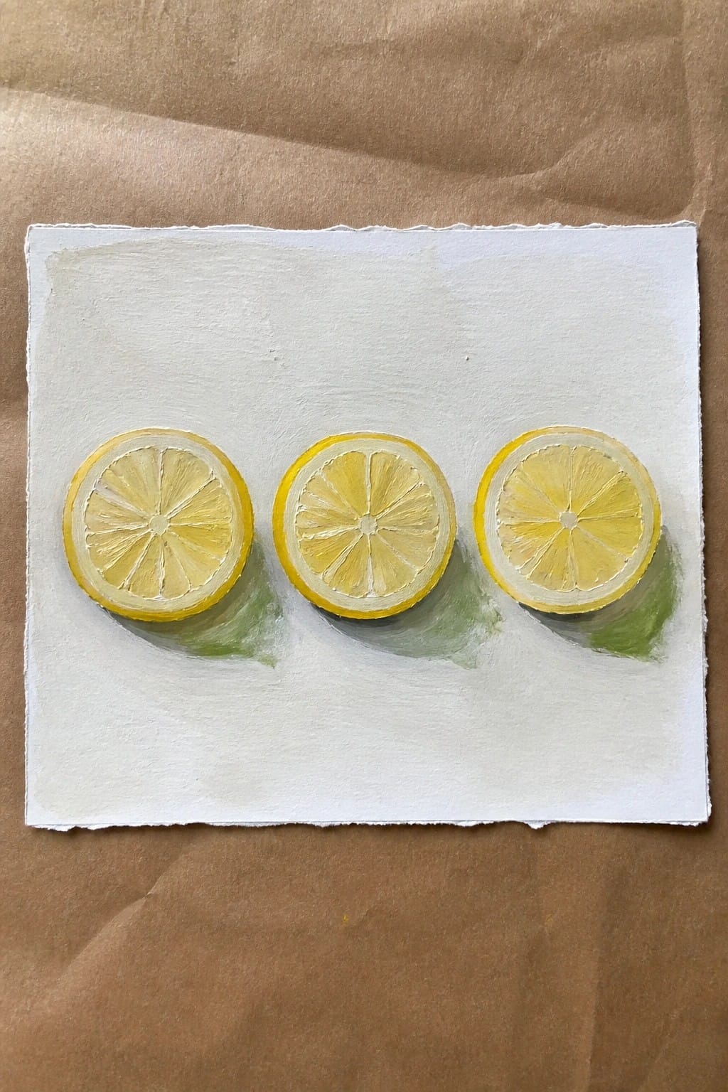 Three yellow lemon slices painted in a row on white paper with green shadows