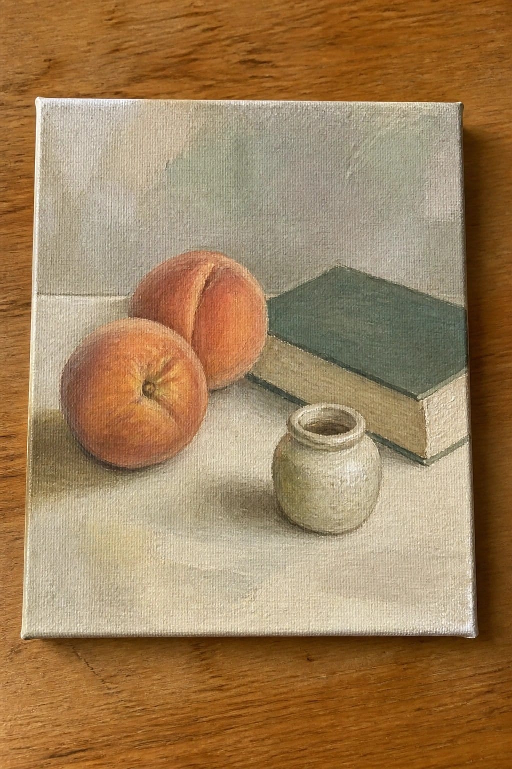 Still life with two peaches, small ceramic jar, and green book on table
