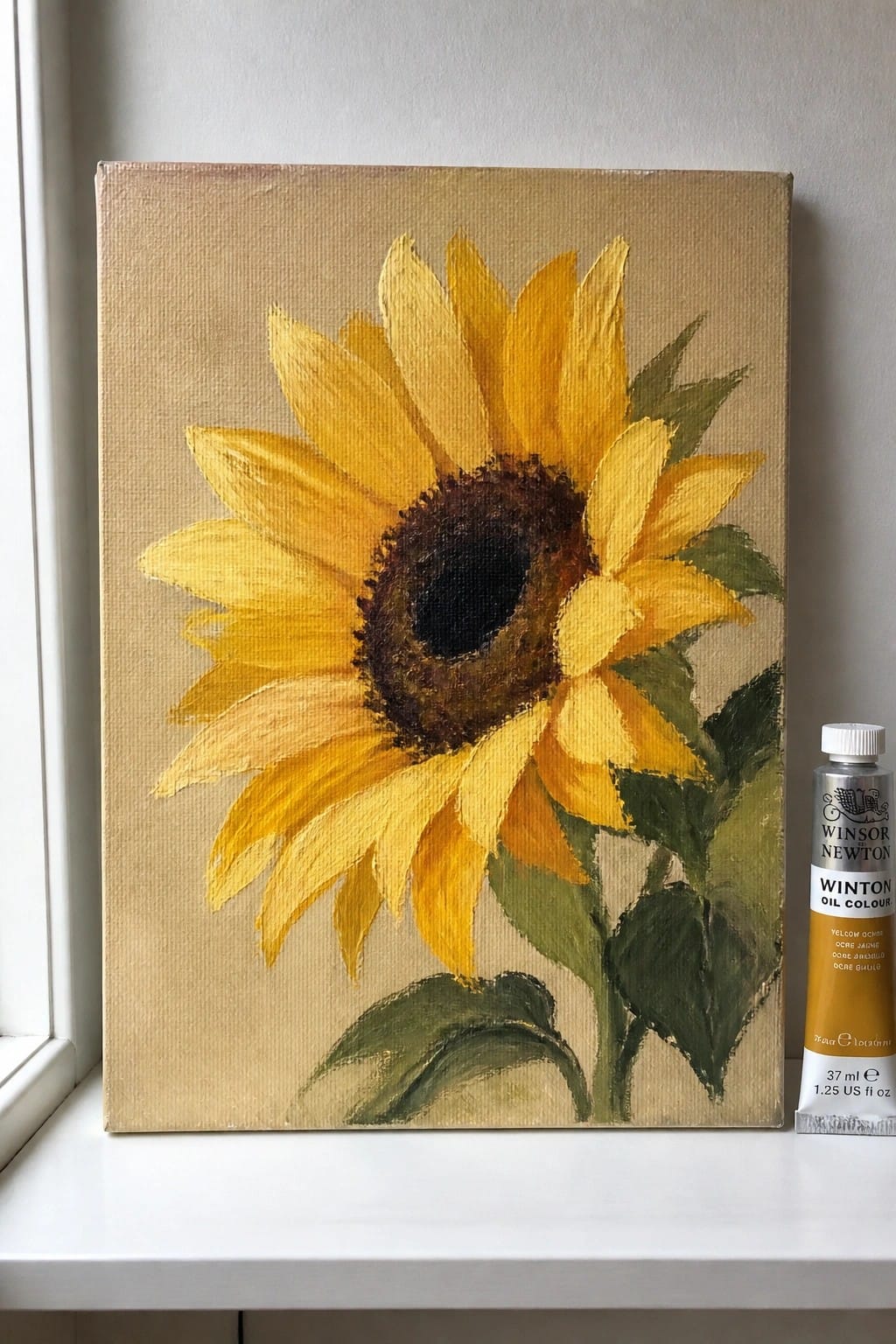Yellow sunflower oil painting on canvas beside yellow ochre paint tube on windowsill
