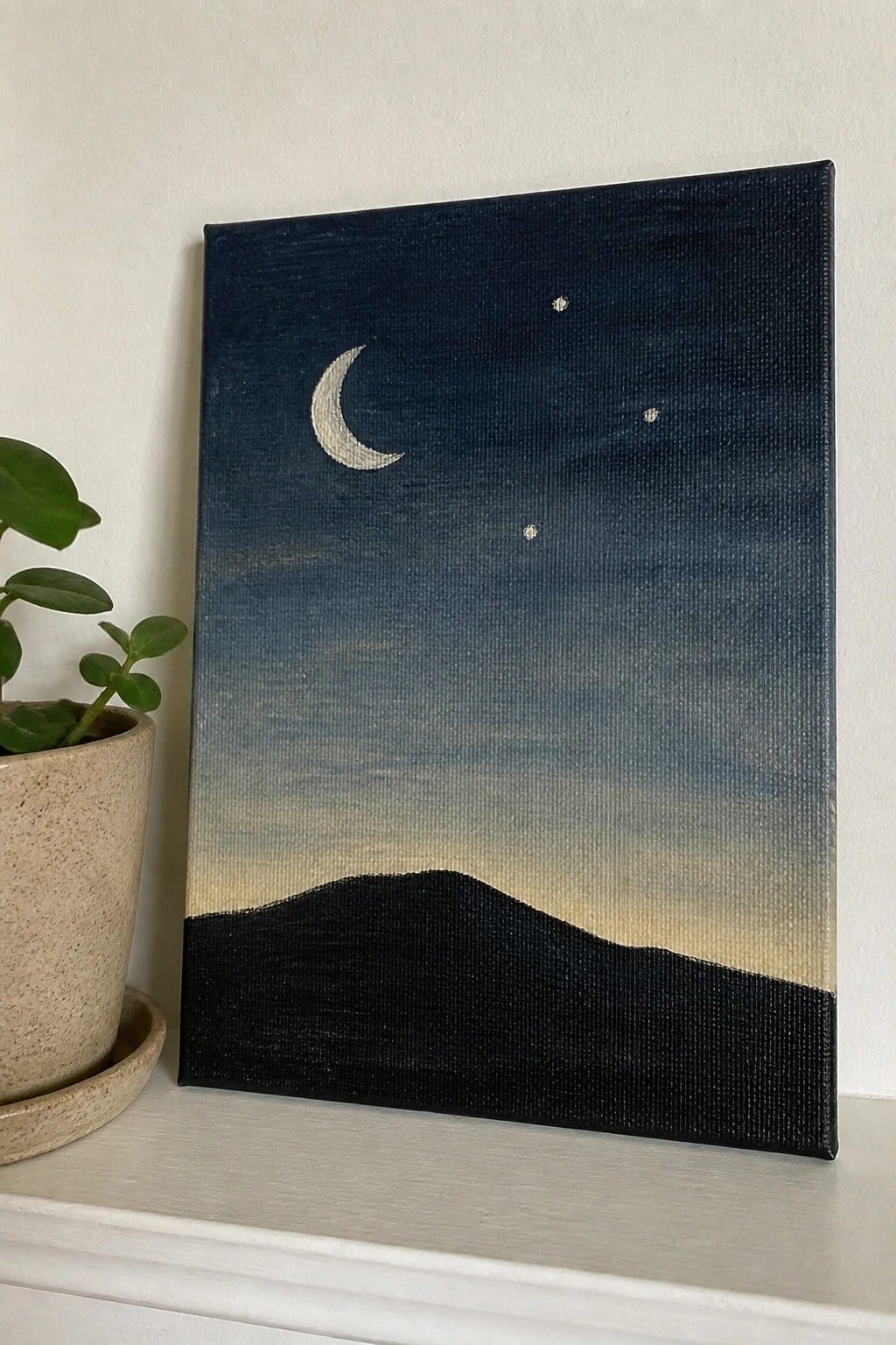Canvas painting of crescent moon and stars above black hills beside potted plant