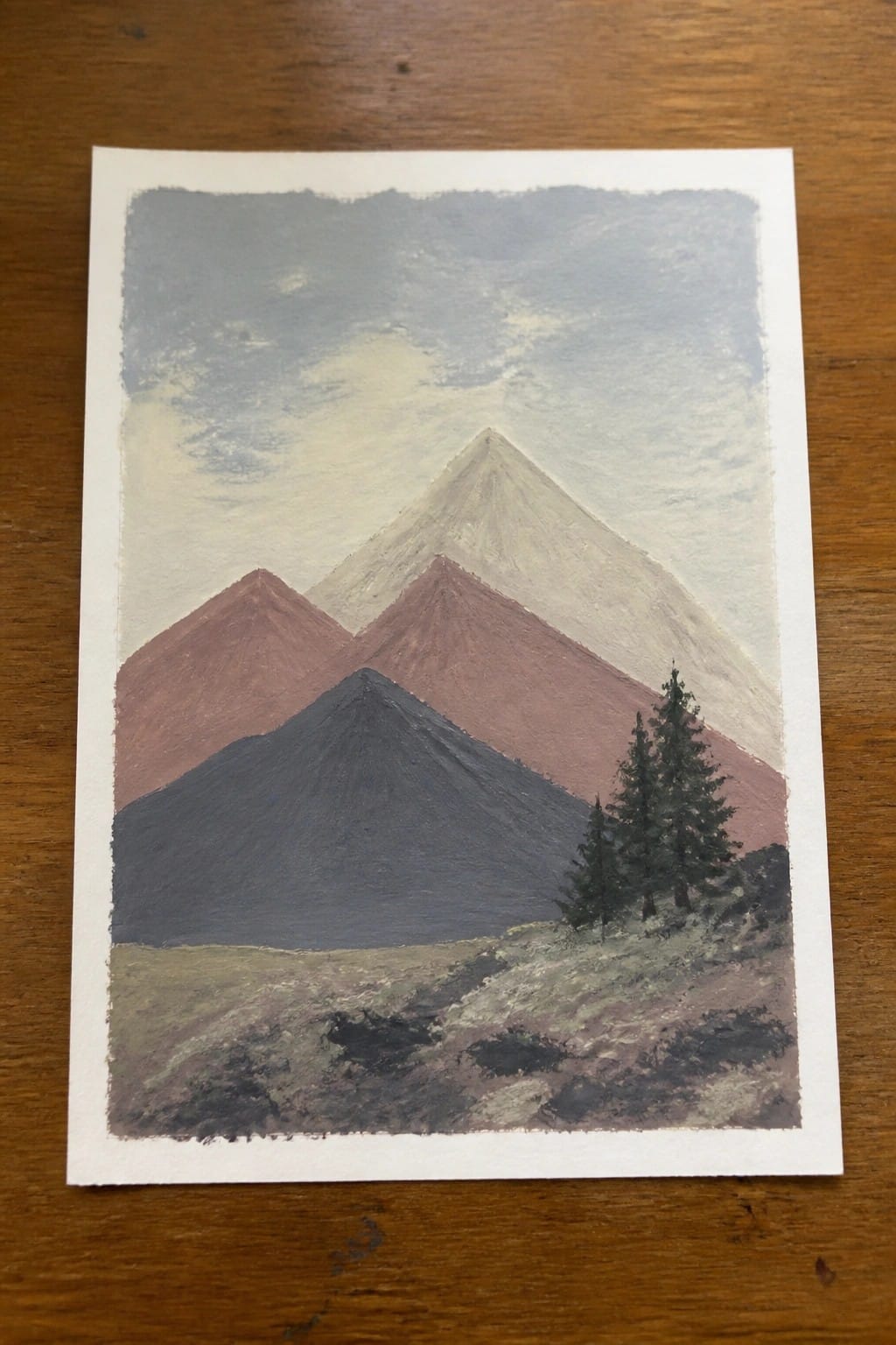 Three painted mountains in brown, red, and blue tones with pine trees and cloudy sky