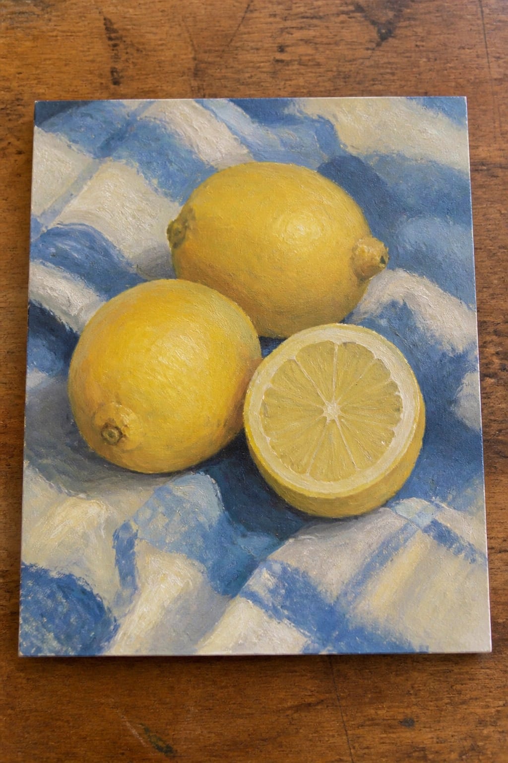 Two whole yellow lemons and one sliced half on blue checkered cloth
