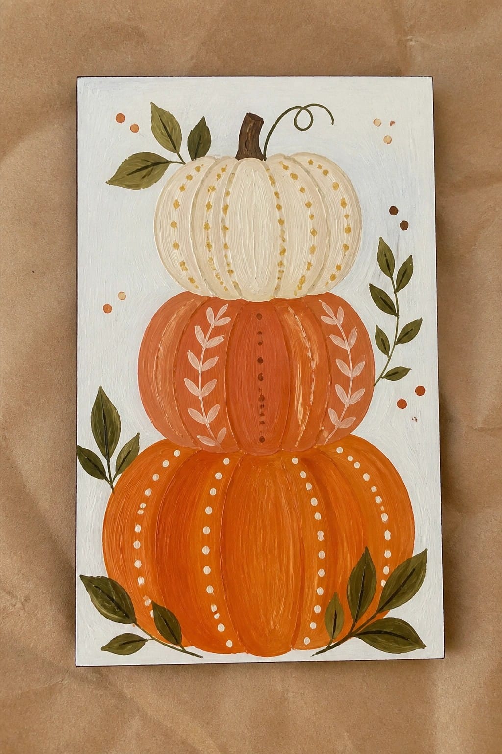 Three stacked orange and white pumpkins with green leaves and dotted accents