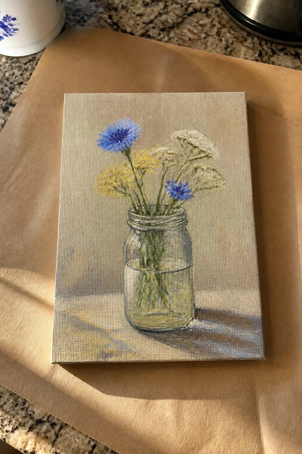 Painting of blue, yellow and white flowers in a glass mason jar on brown paper