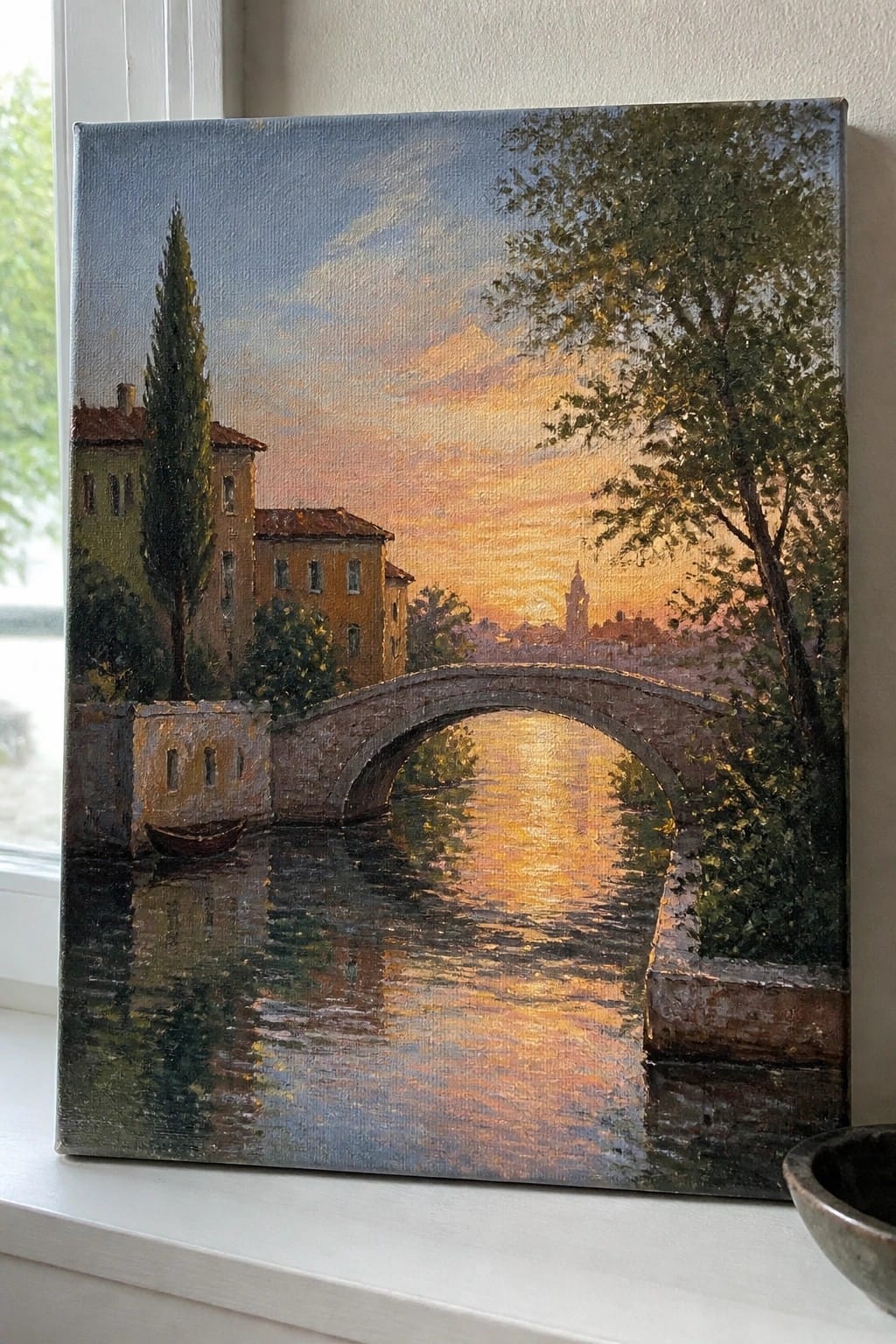Oil painting of arched stone bridge over sunset river with buildings and trees.