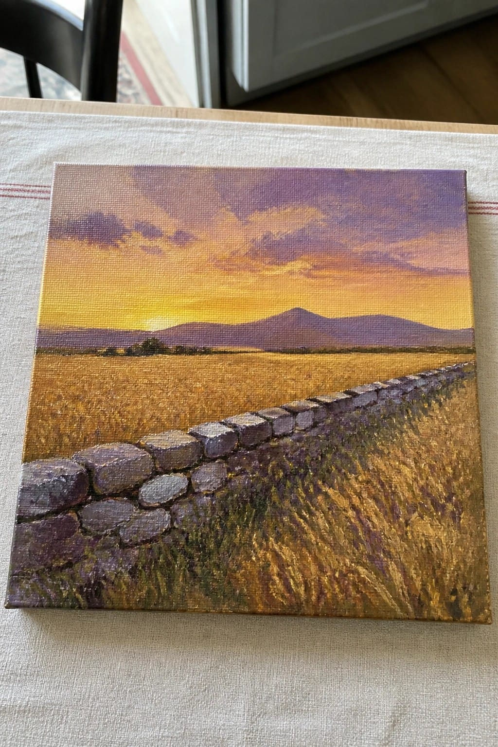 Sunset landscape painting with stone wall across golden field on white tablecloth