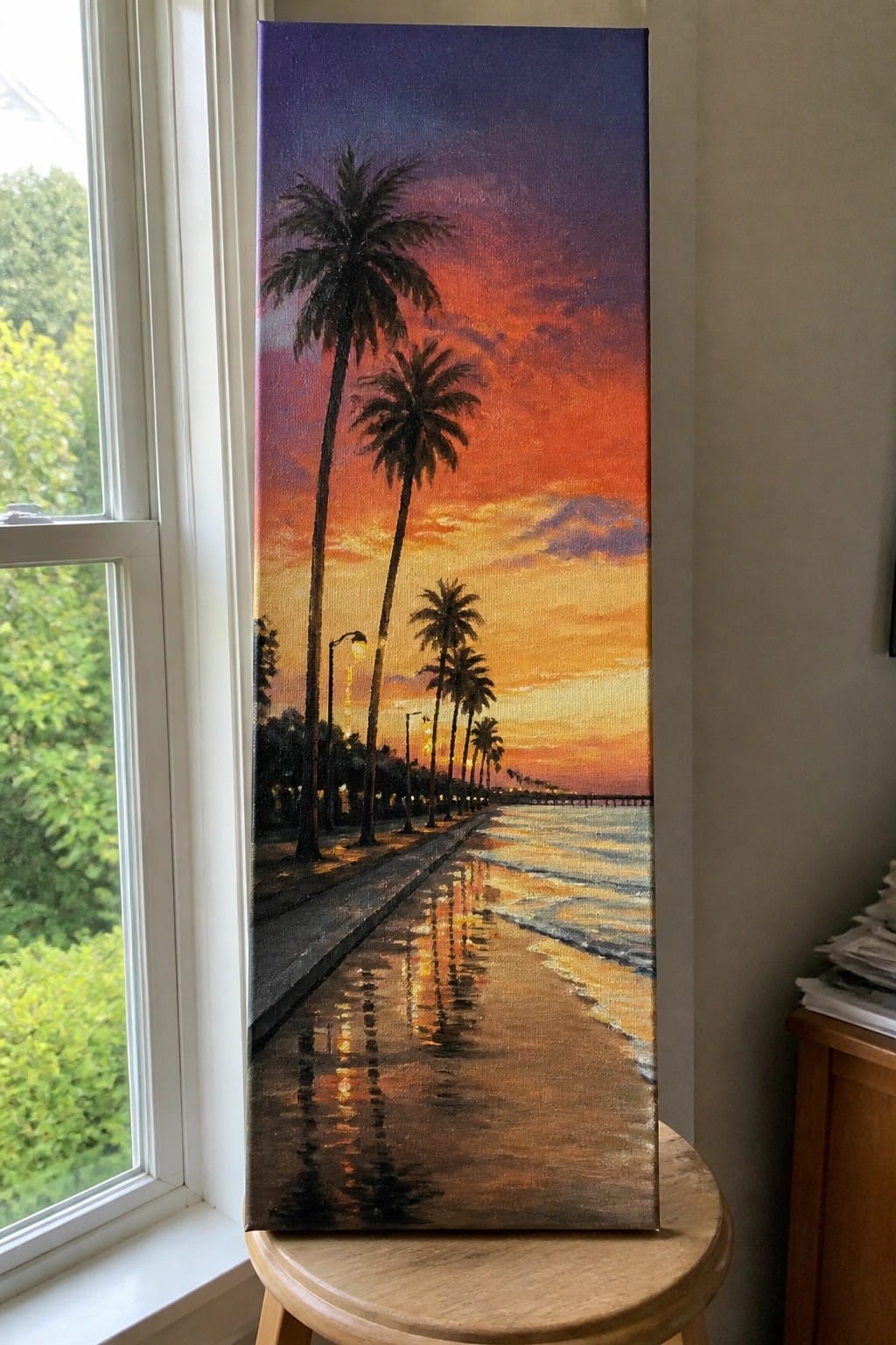 Vertical painting of vibrant sunset beach with palm trees on wooden stool by window