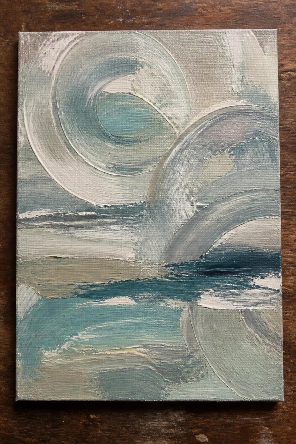 Abstract painting with swirling teal, gray, and white circular brushstrokes over layered waves on wood.