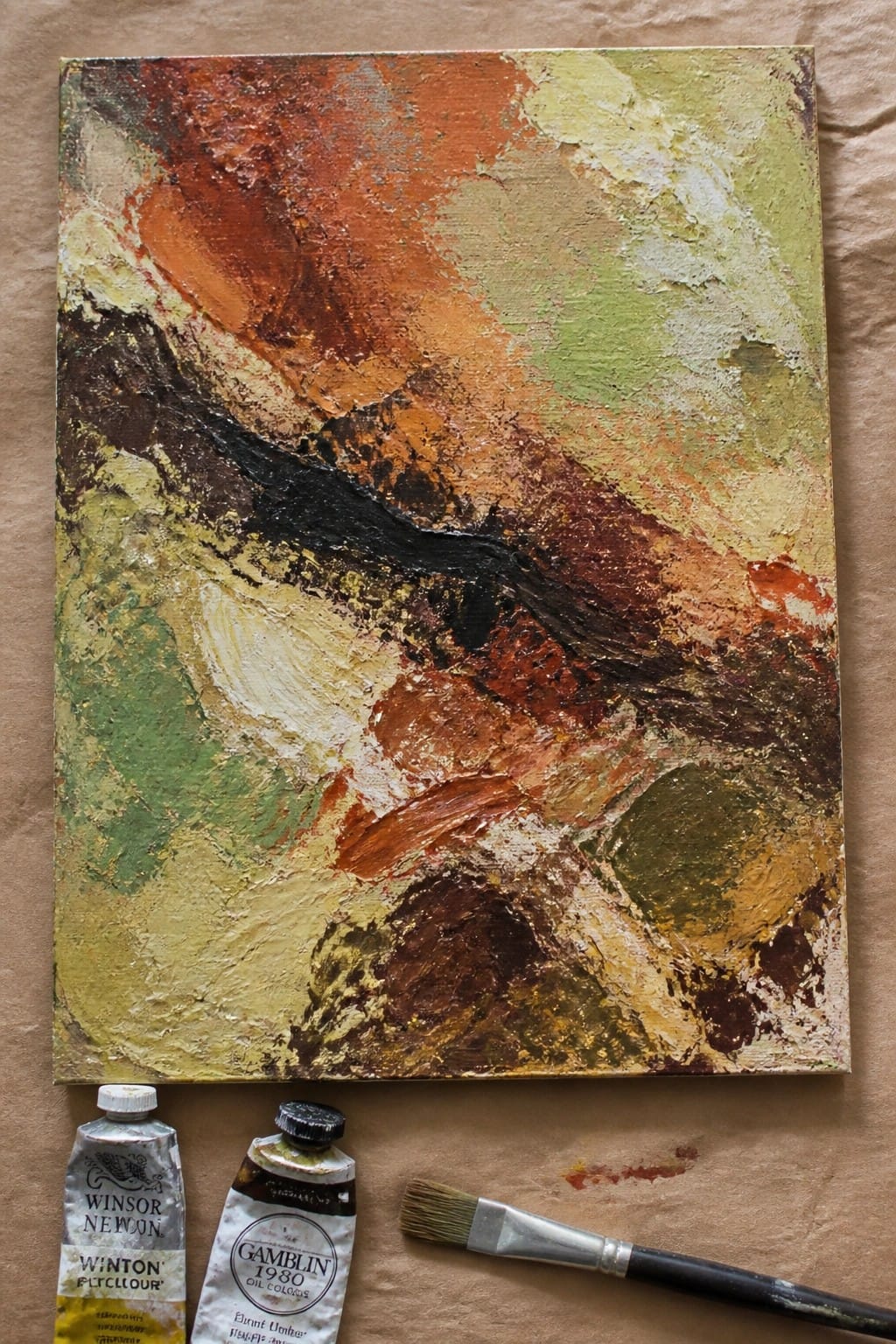 Abstract painting in orange, green, brown hues with paint tubes and brush.
