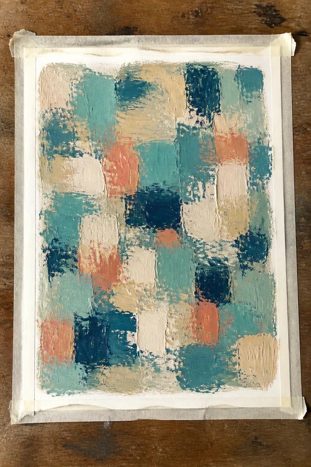 Abstract oil painting taped to wood, showing thick textured strokes in teal, coral, navy, beige, and white forming an irregular grid.