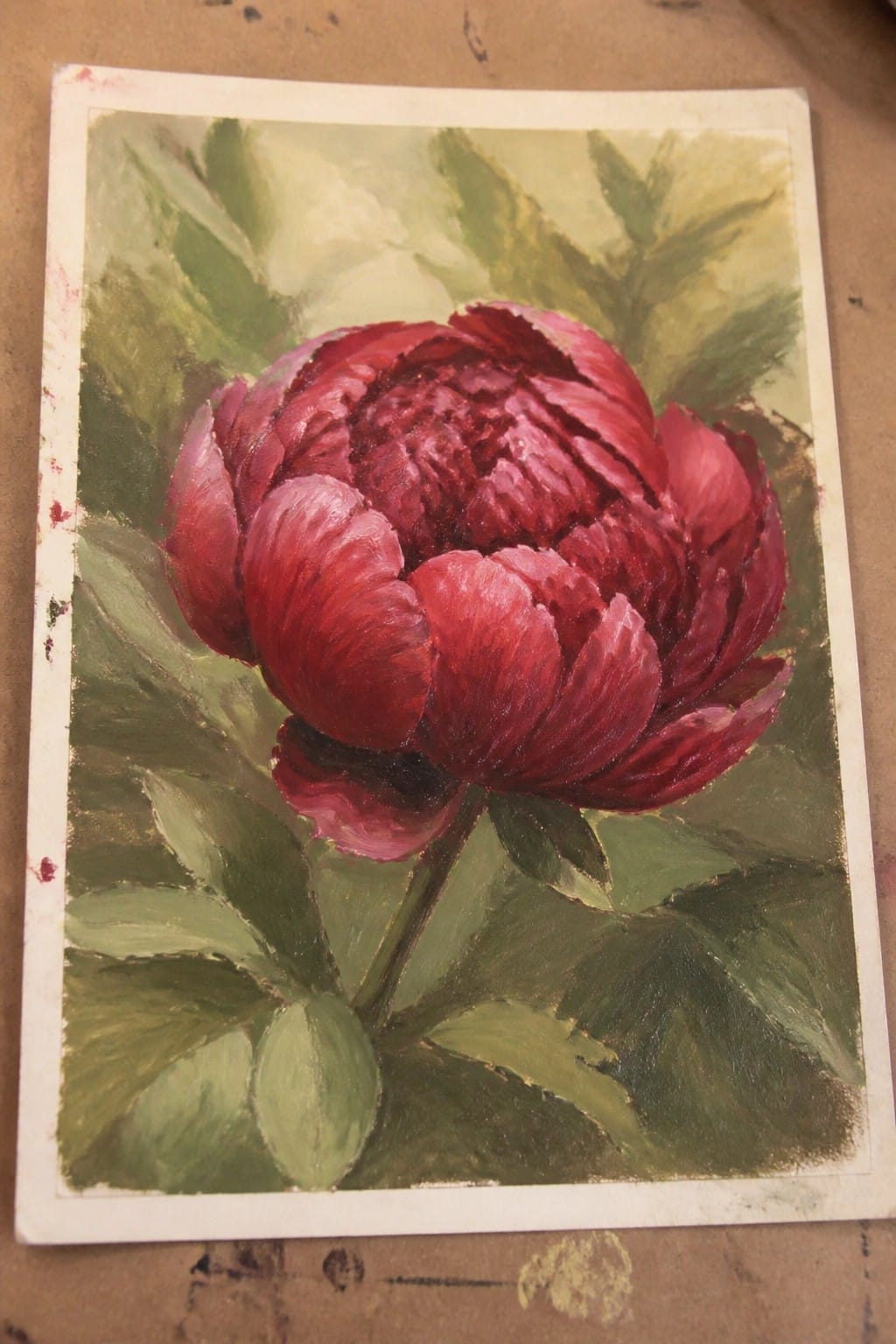 Rich red peony with layered petals amid green leaves in oil painting