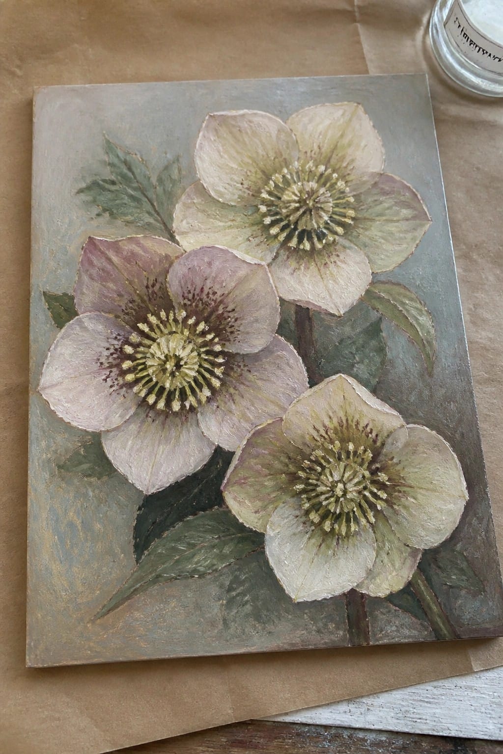 Realistic oil painting of three hellebore flowers in pale pink and cream with green centers and dark leaves against a muted background.