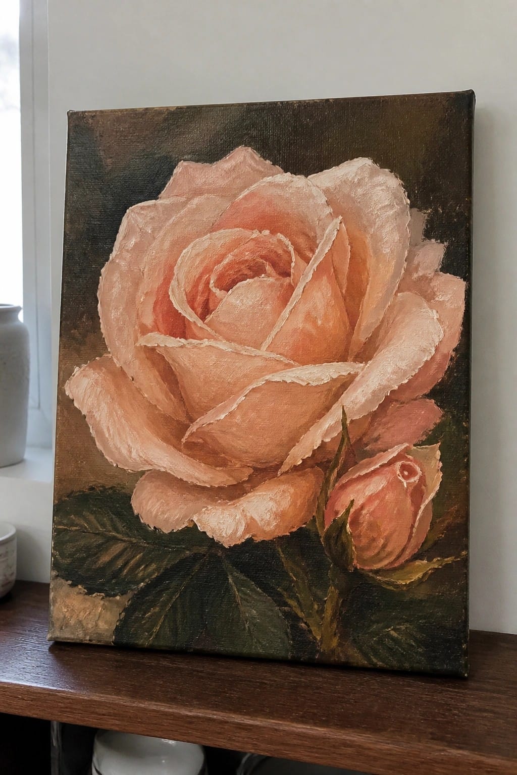 Realistic oil painting of a large pink rose with a smaller bud and dark green leaves on a textured dark background, resting on a wooden surface.