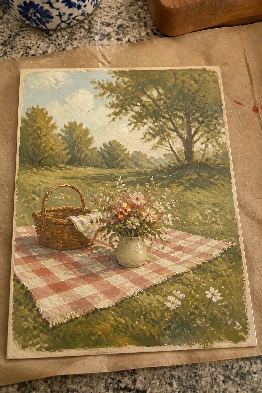 Red checkered picnic blanket with basket and wildflower pitcher in grassy meadow