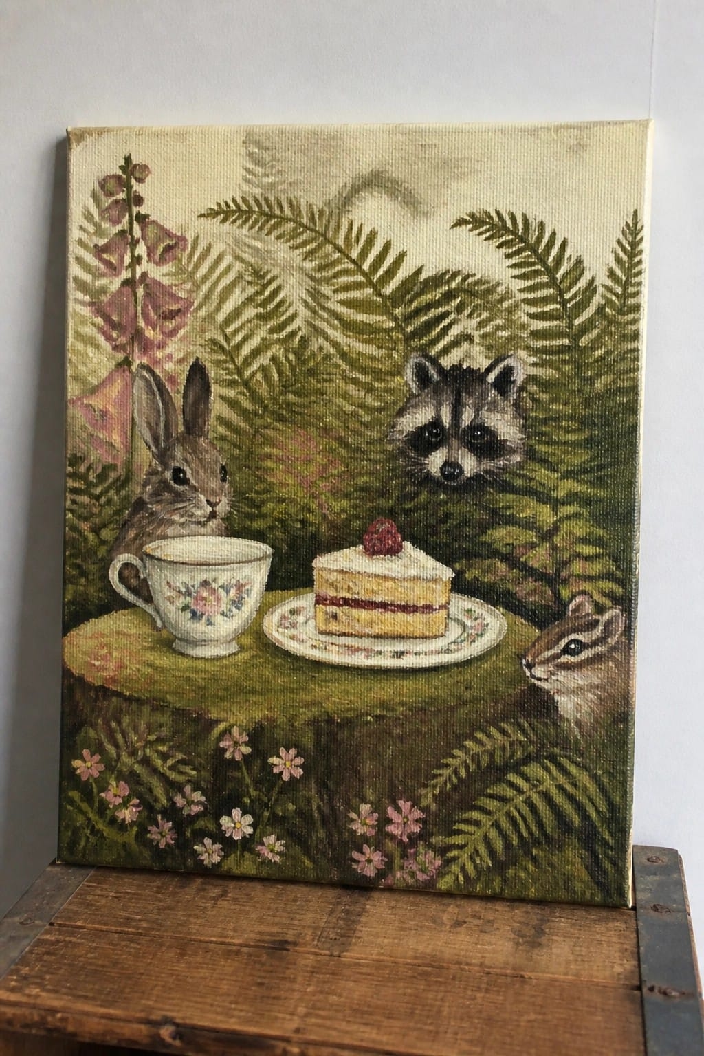 Whimsical painting of rabbit, raccoon, and chipmunk at cake tea party on forest stump
