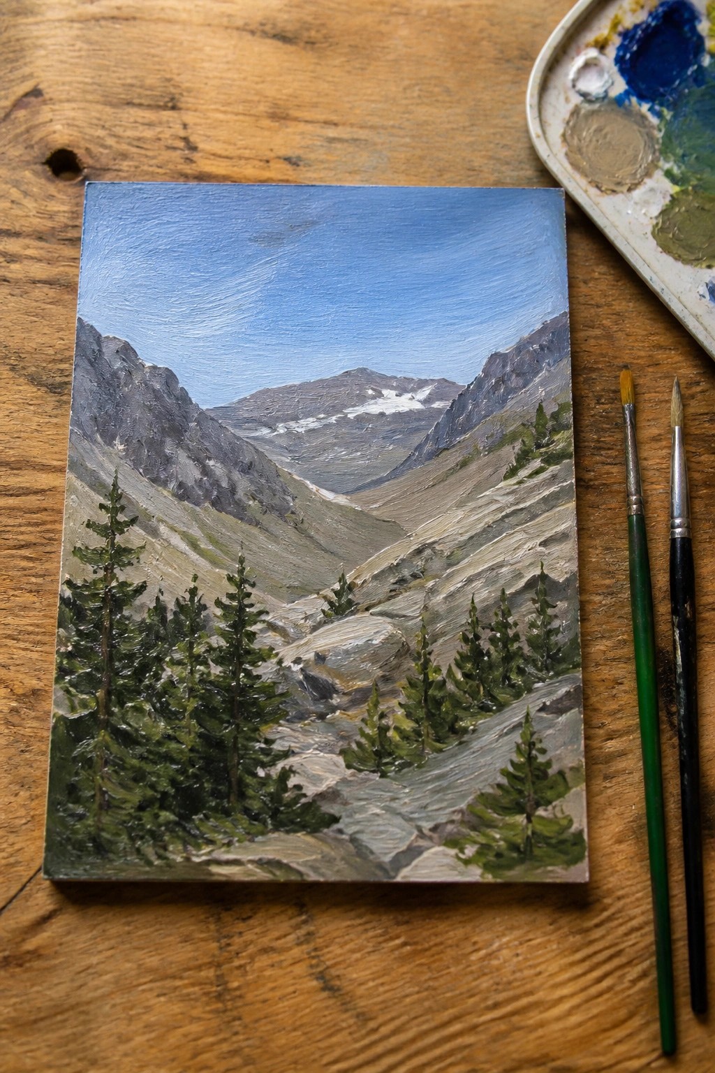 Mountain landscape painting on wooden table with palette and brushes