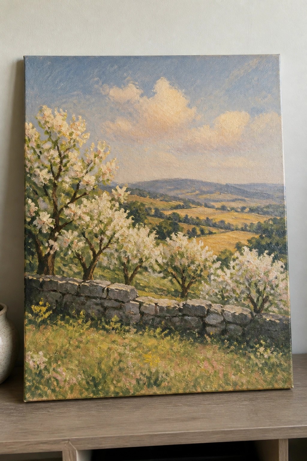Stone wall borders blooming white trees overlooking rolling yellow-green hills under a blue sky.