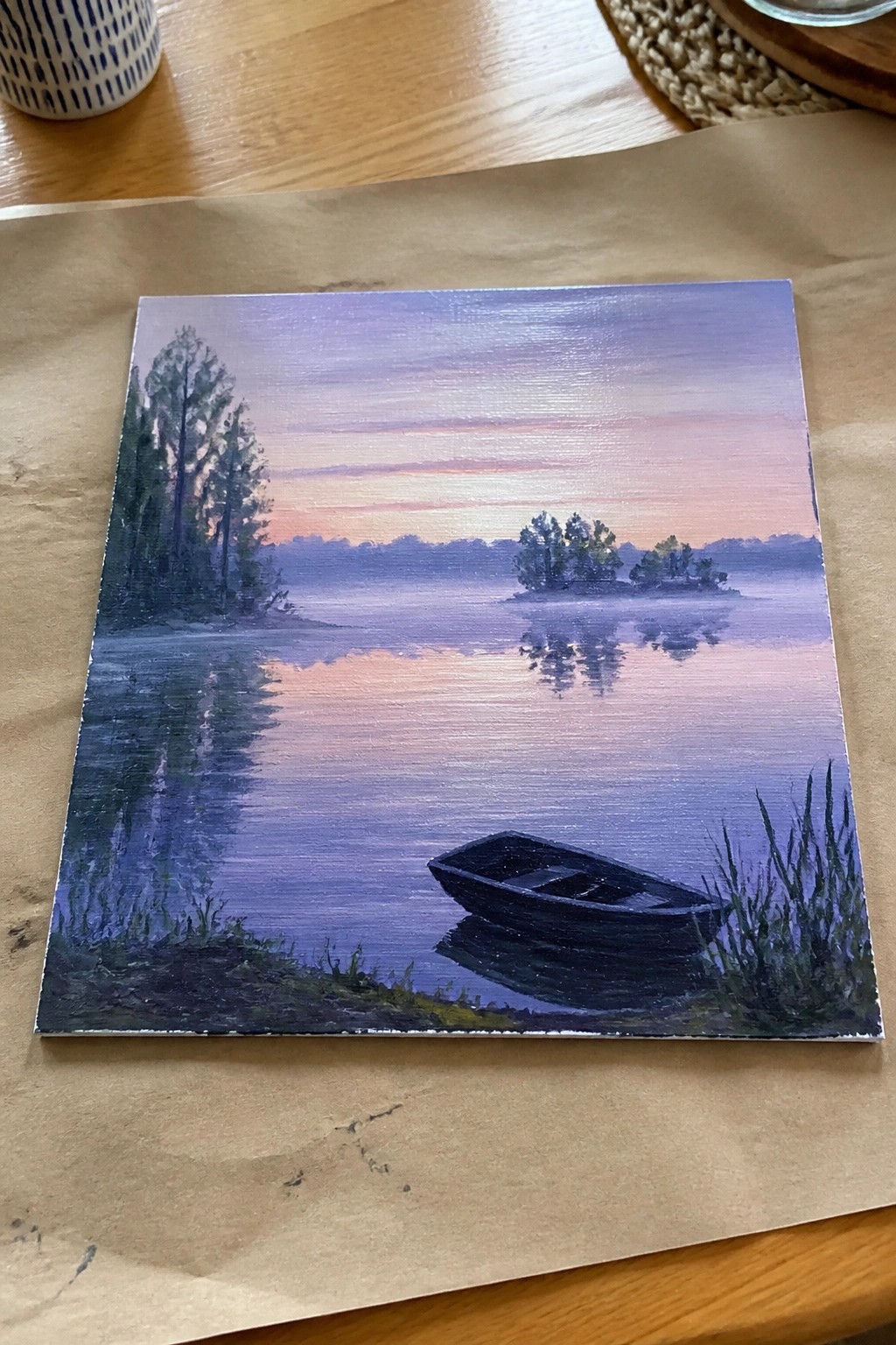Landscape painting of misty purple lake at sunset with dark boat on shore.