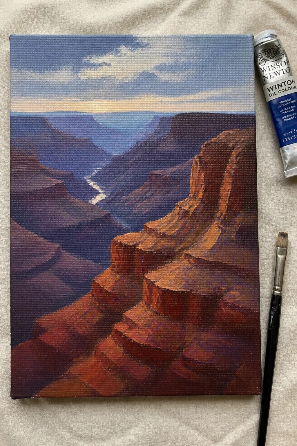 Grand Canyon oil painting on canvas beside ultramarine paint tube and brush.