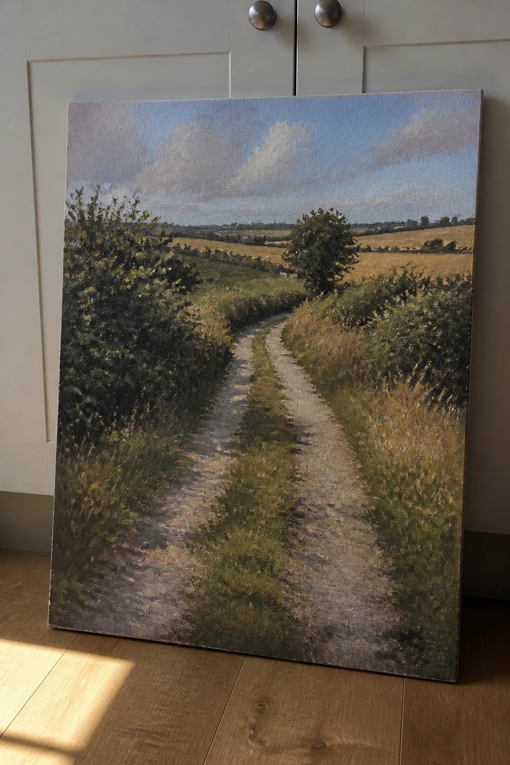 Winding dirt path through green fields in landscape painting against white cabinets