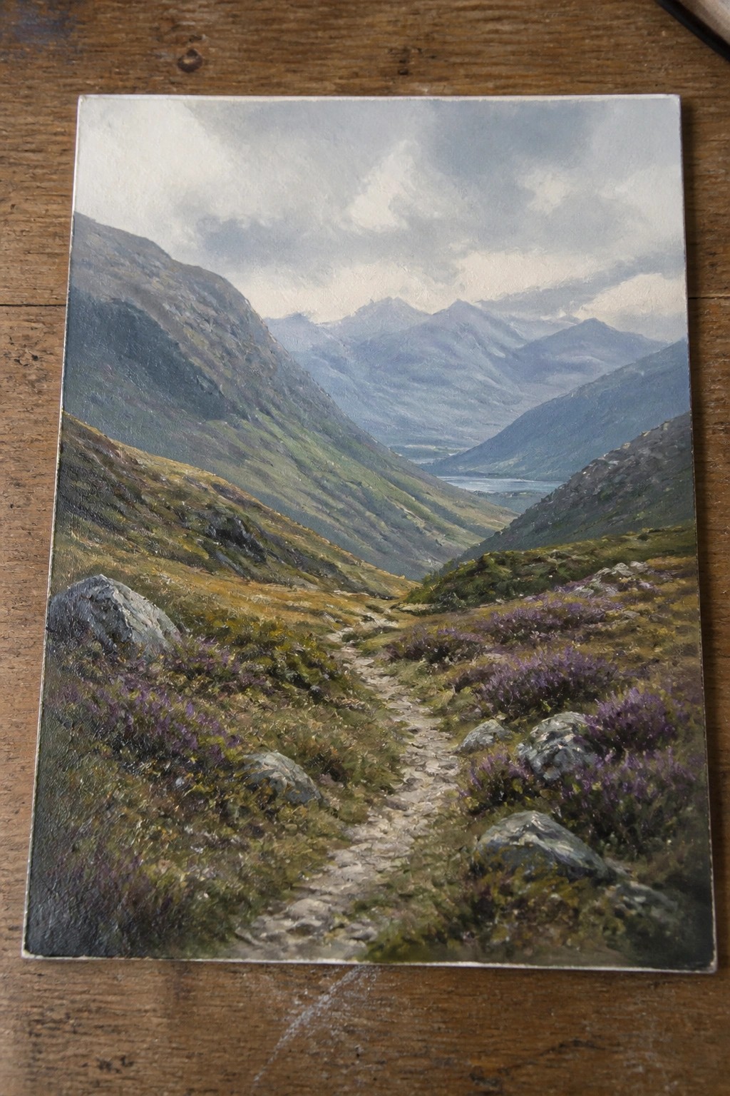 Winding rocky path through purple heather hills toward misty mountains and distant lake