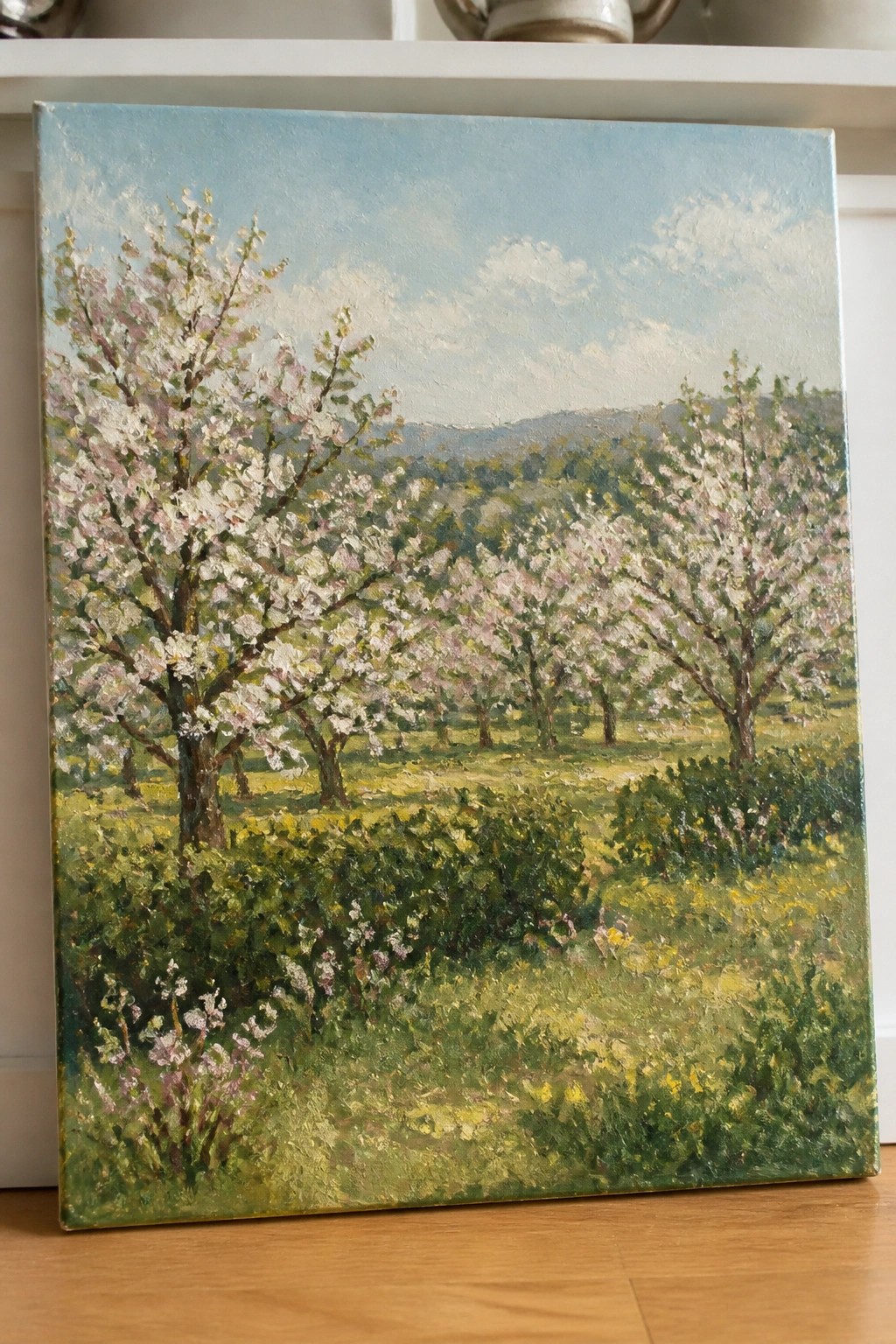 Oil painting of blooming cherry trees in a green meadow with rolling hills.