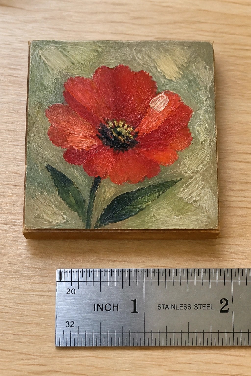 Small red poppy painting on wood beside inch-marked metal ruler.