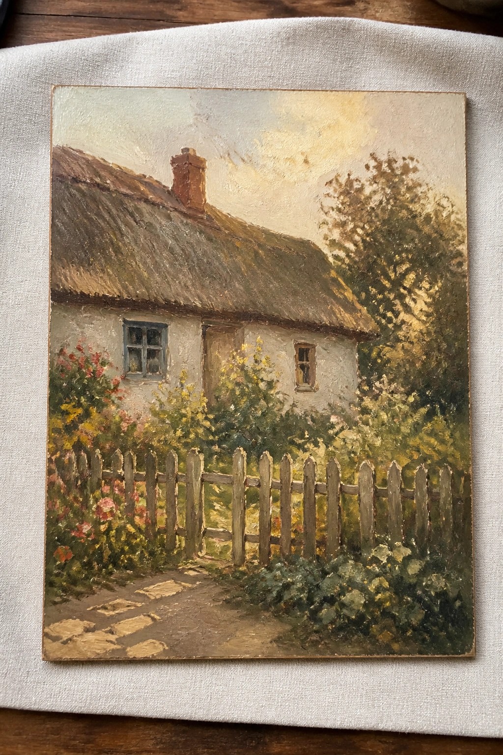 Thatched cottage with wooden fence, colorful flowers, and stone path at sunset.