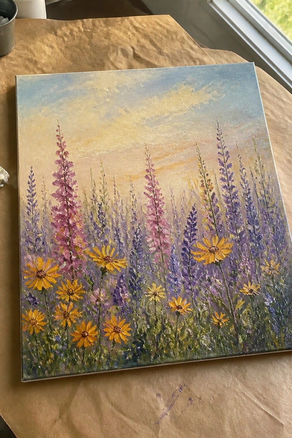 Vivid painting of yellow daisies and tall purple-pink flowers under a golden sky.