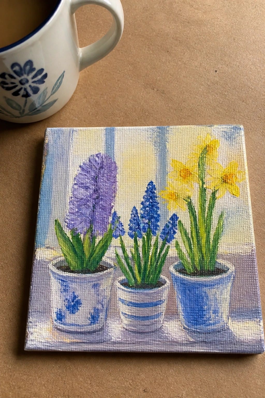 Small painting of purple blue and yellow potted flowers beside a white mug