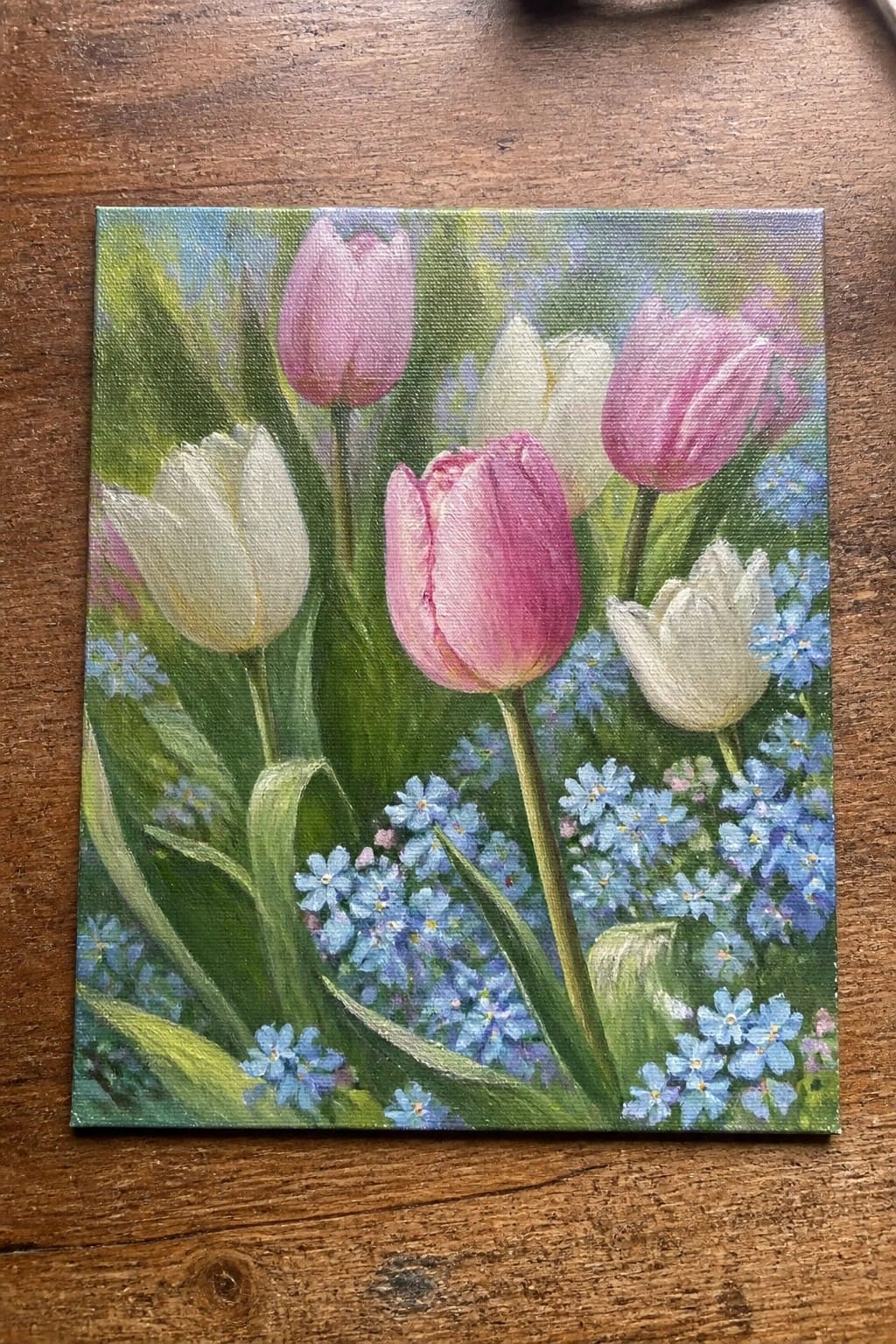 Vibrant painting of pink and white tulips amid clusters of blue forget-me-nots on canvas