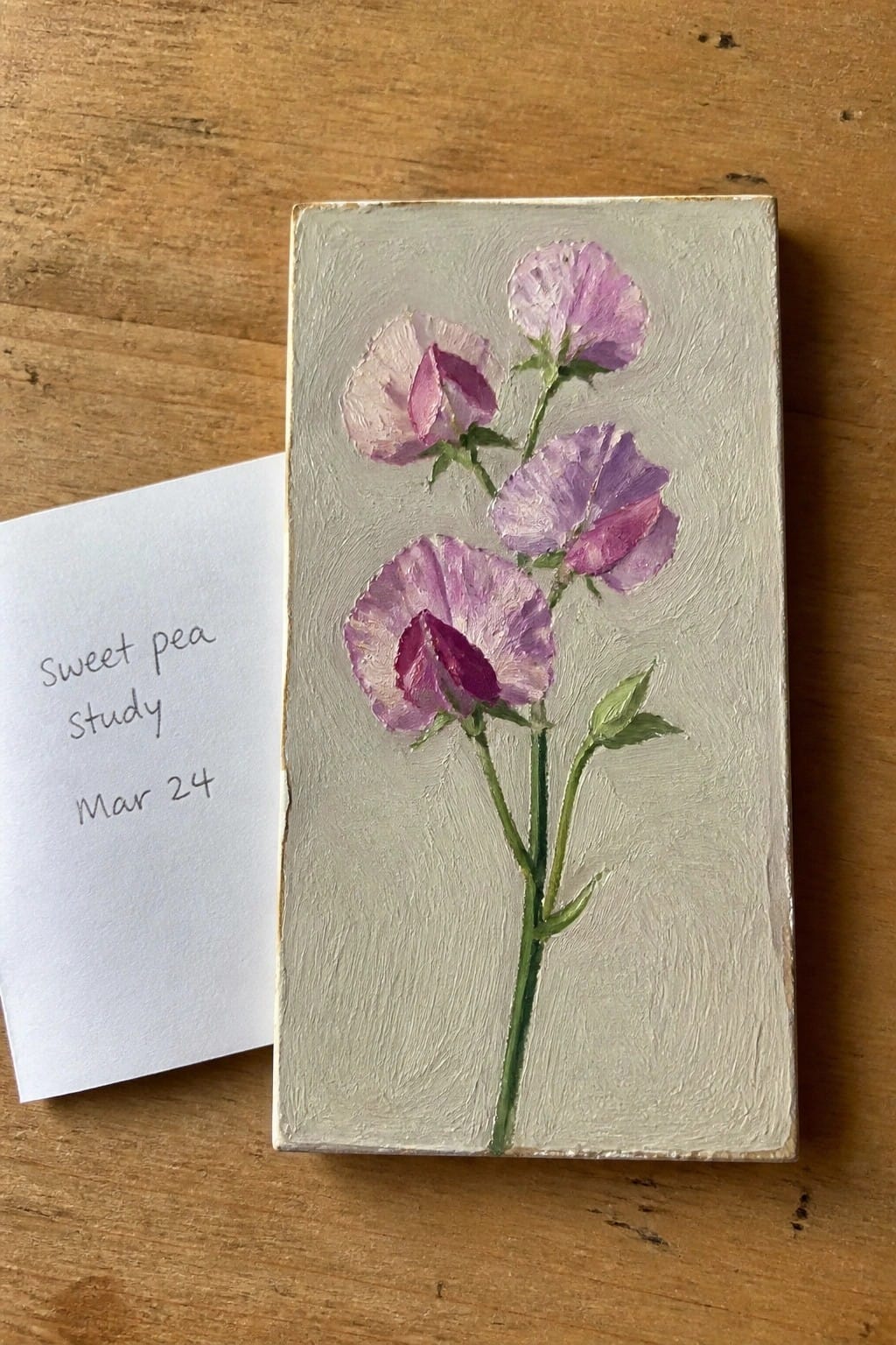 Small painting of purple sweet peas beside handwritten study card on wood