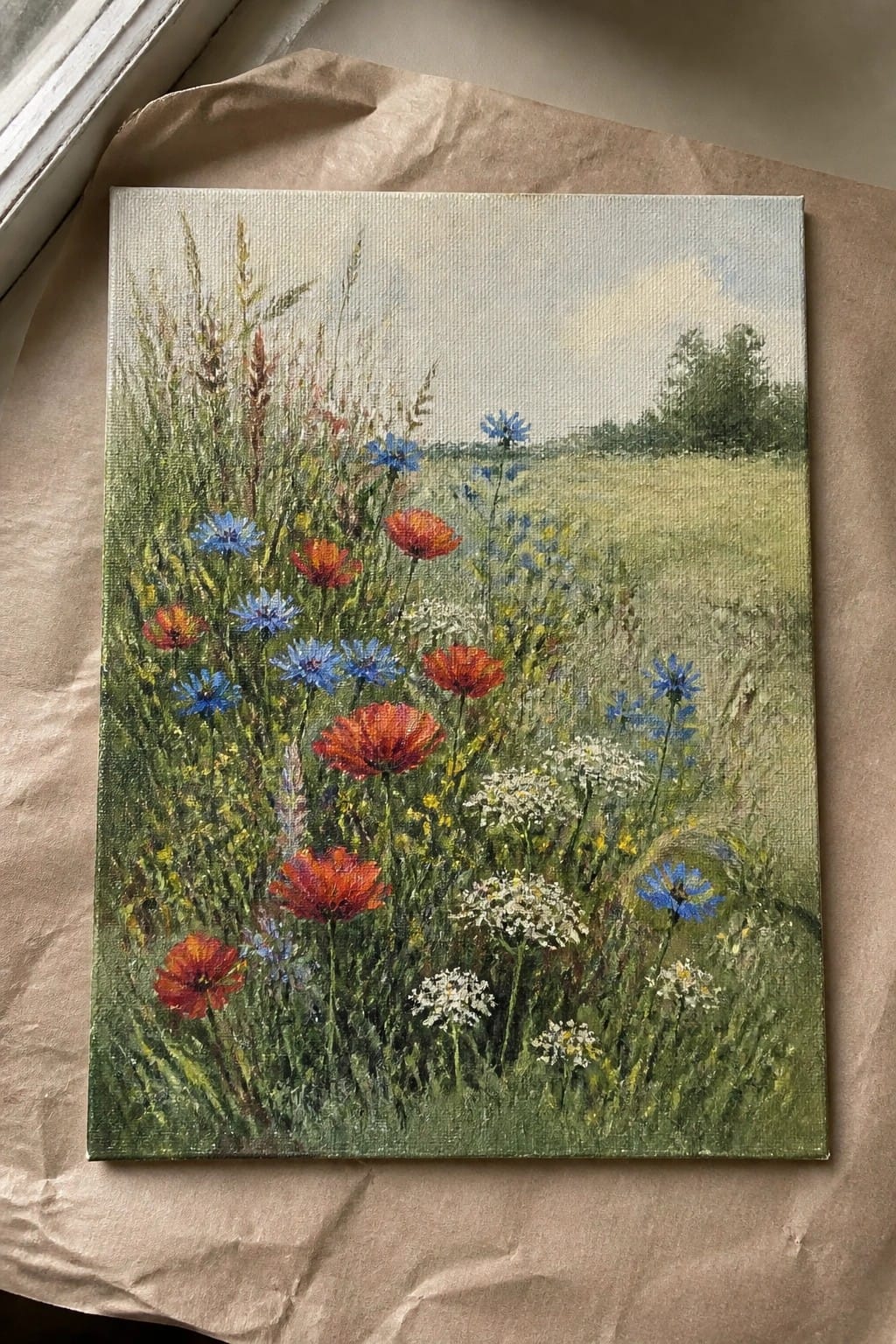Canvas painting of wildflower meadow with red poppies, blue cornflowers, and white blooms.