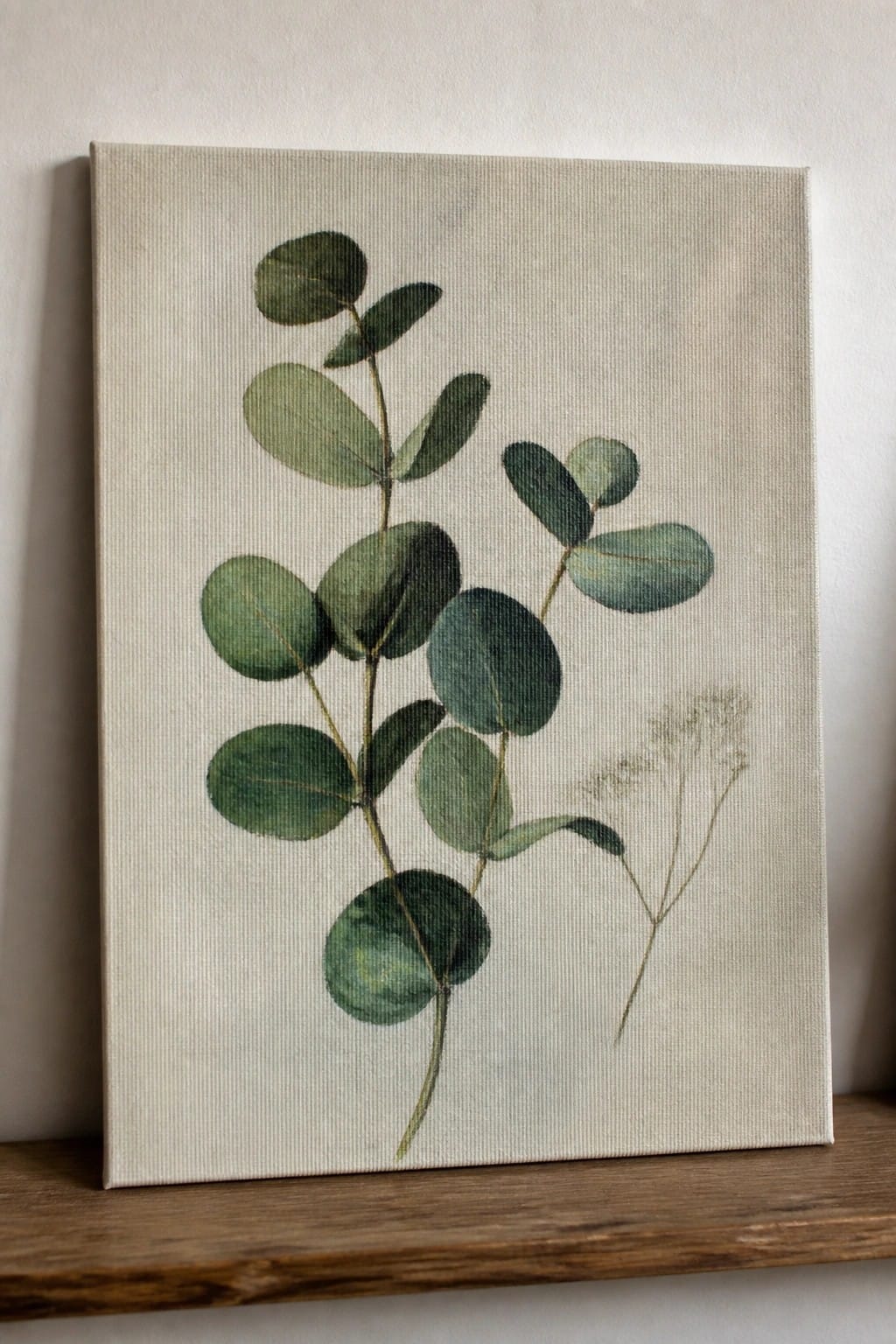 Watercolor eucalyptus branches with green leaves on beige canvas above wooden shelf.