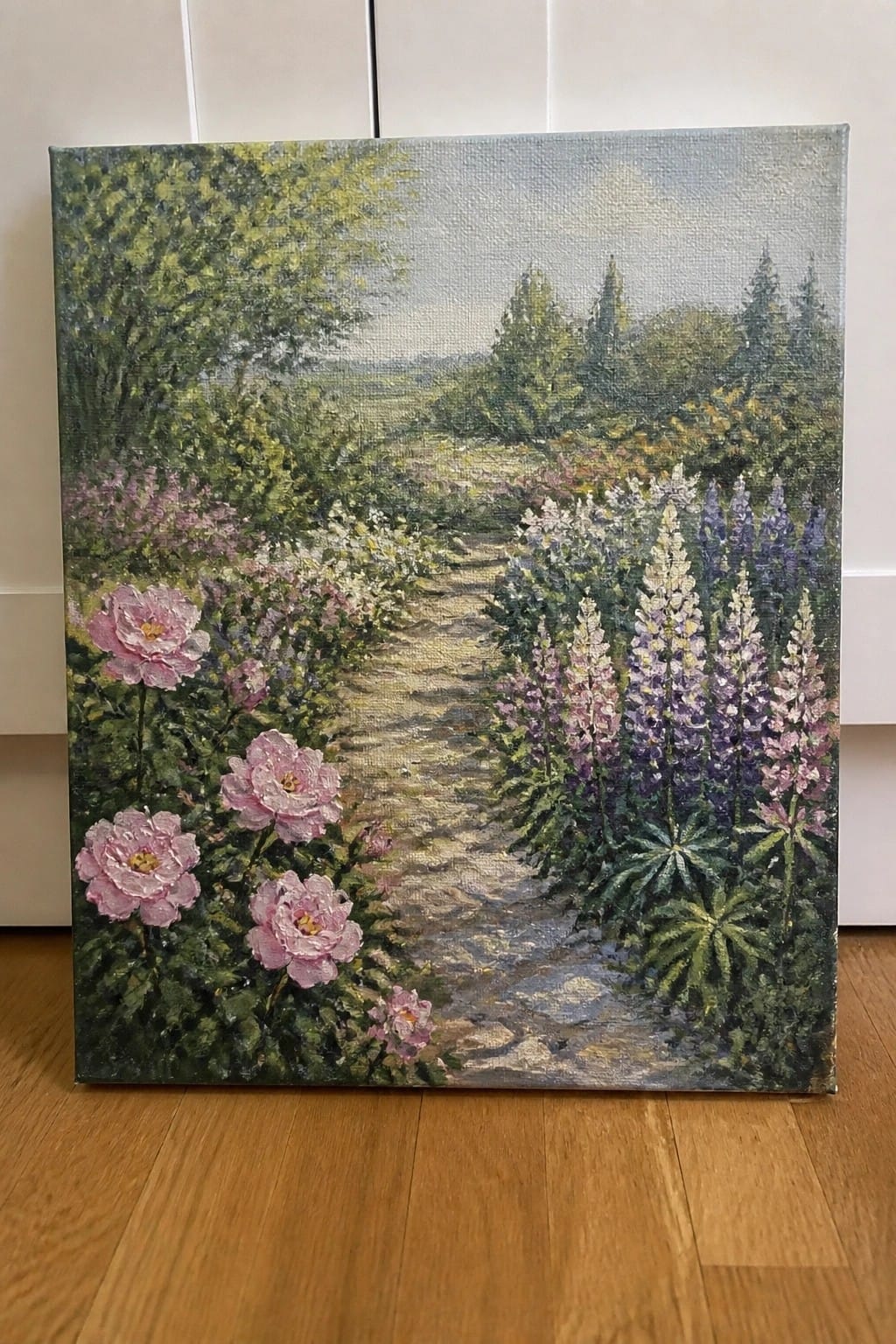 Winding dirt path lined with pink roses and tall purple lupines amid lush greenery.