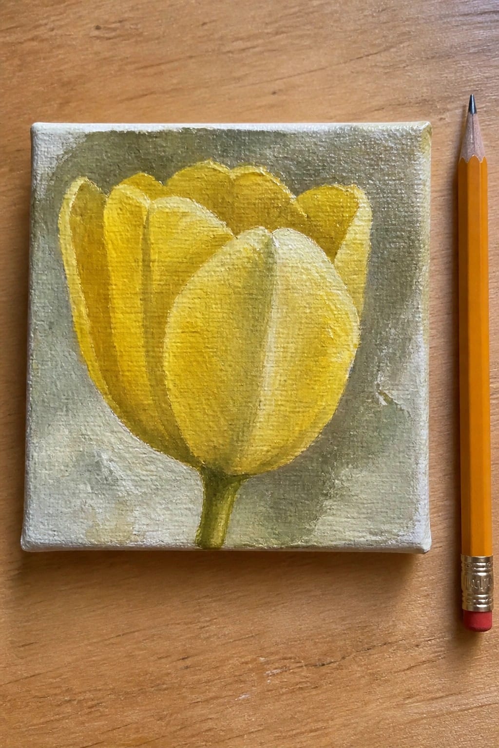 Yellow tulip painting on small canvas beside yellow pencil on wood