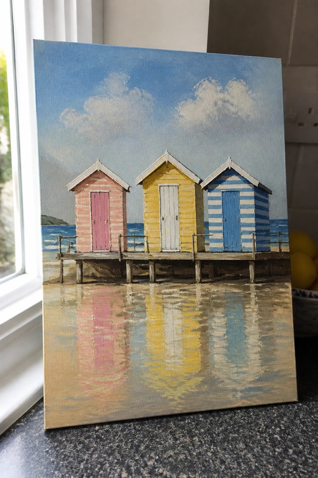 Three colorful beach huts on pier with reflections in calm water below