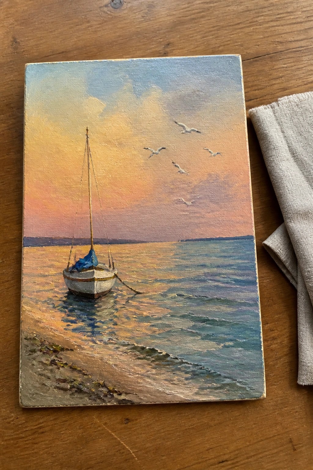 Impressionistic painting of sailboat on beach at vibrant sunset with flying seagulls