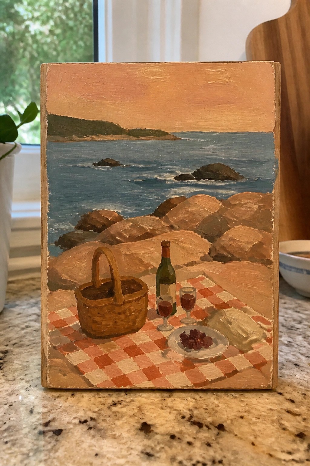 Red checkered picnic blanket with basket, wine and glasses on rocky ocean shore