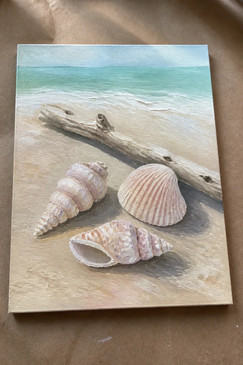 Realistic painting of three seashells and driftwood on sandy beach with turquoise ocean waves.