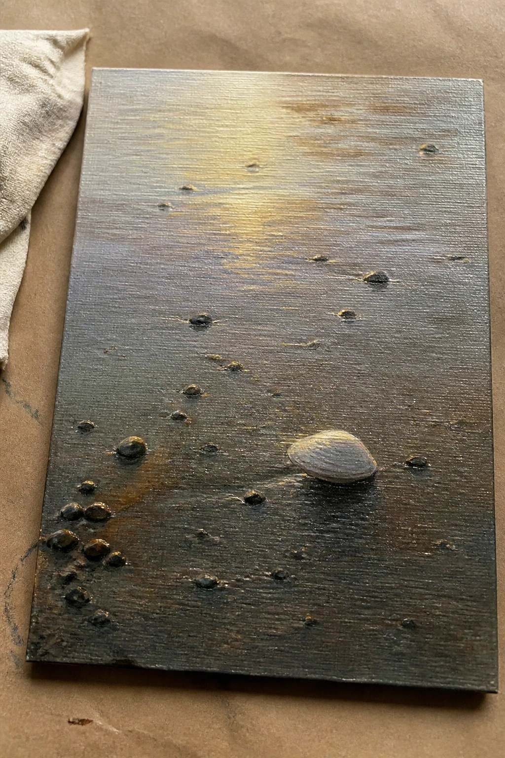 Dark wooden panel with scattered pebbles, seashell, and golden light reflection on brown paper