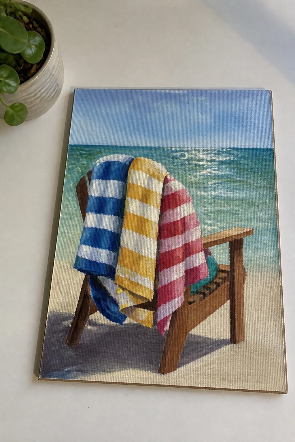 Wooden beach chair draped with blue, yellow, and red striped towels facing ocean.