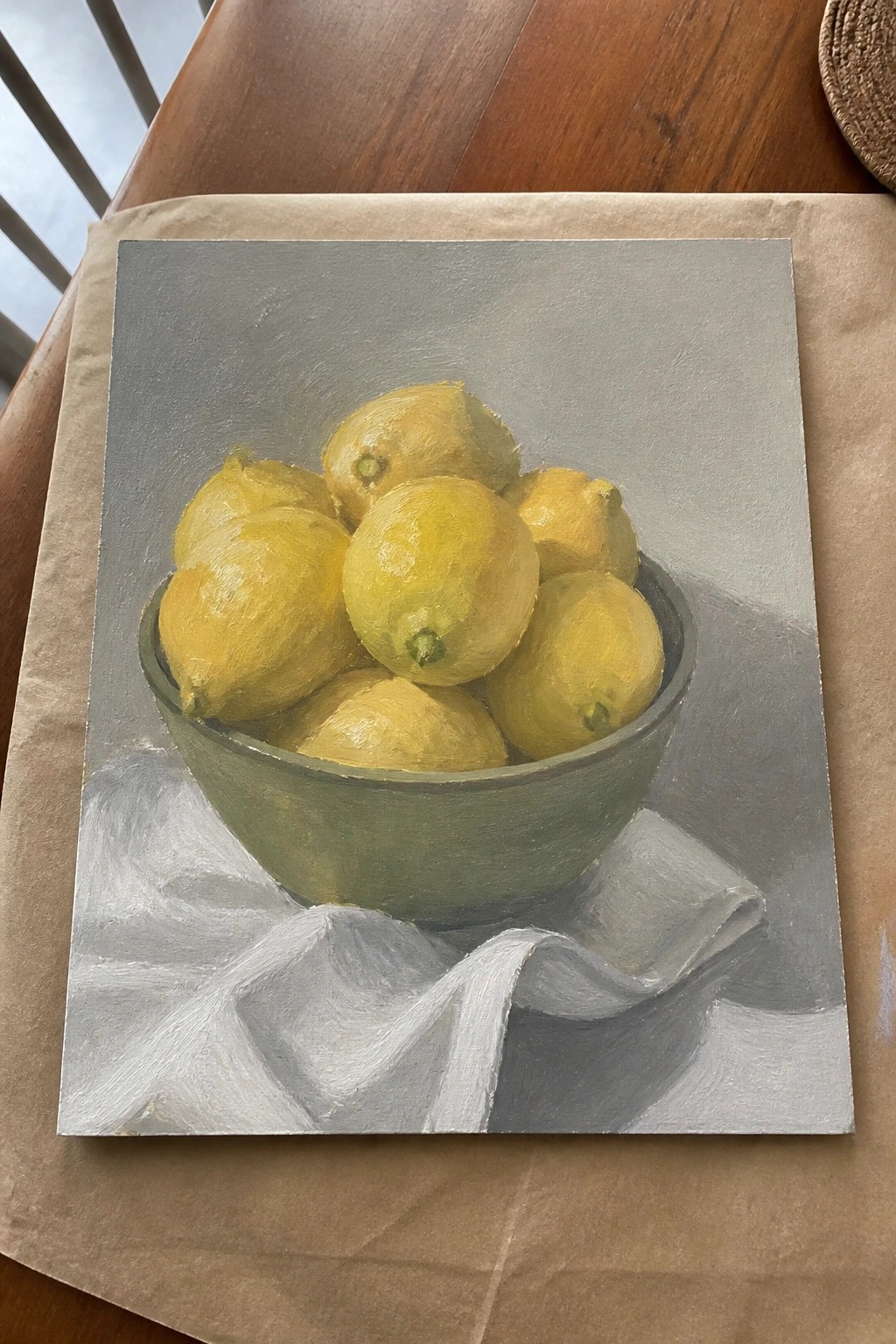 Realistic still life painting of yellow lemons in green bowl on white cloth