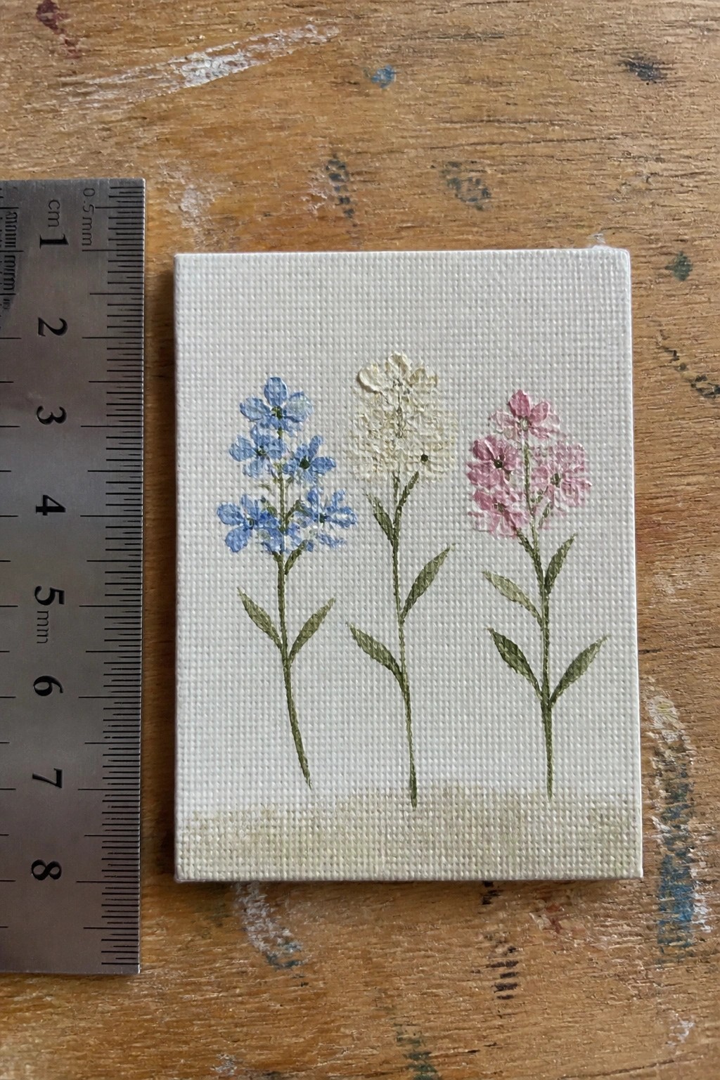 Tiny canvas with blue, white, and pink flower paintings beside metal ruler