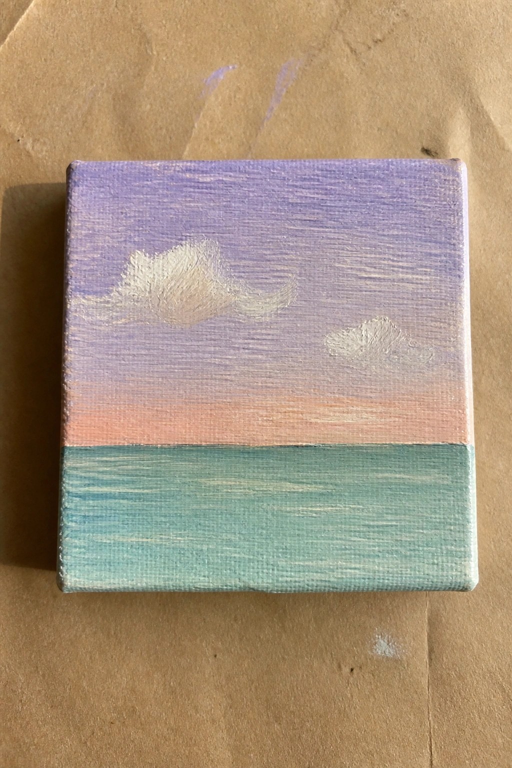 Small square canvas painting of purple sky with clouds over pink sunset and teal water.