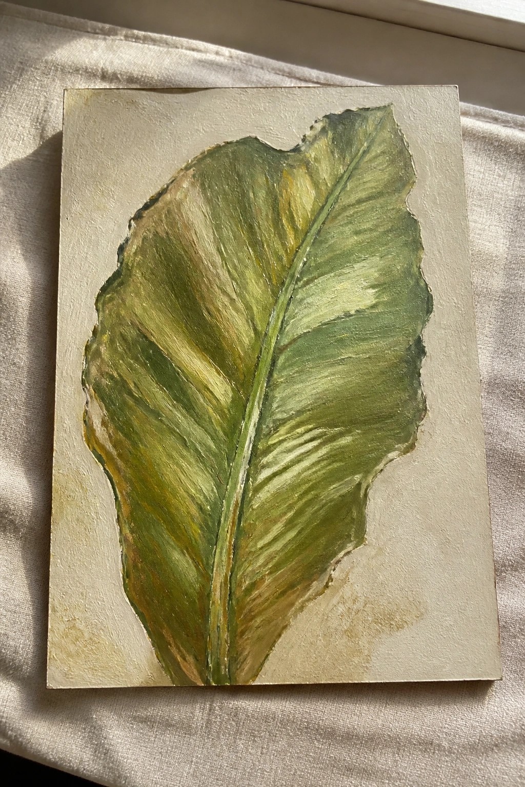 Large green leaf painting with textured brushstrokes on canvas over light fabric